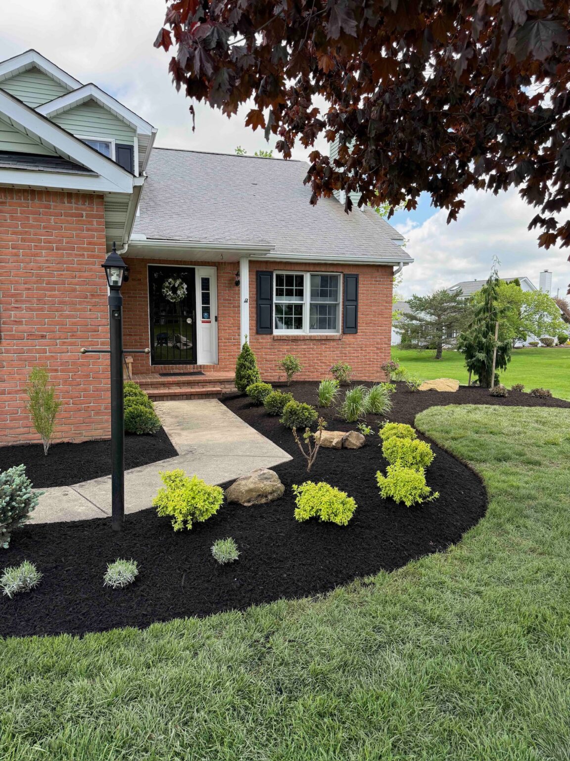 Front walkway landscape design with fresh mulch, shrubs, ornamental plantings, boulders, and lawn edging at a home in Brunswick, Ohio.