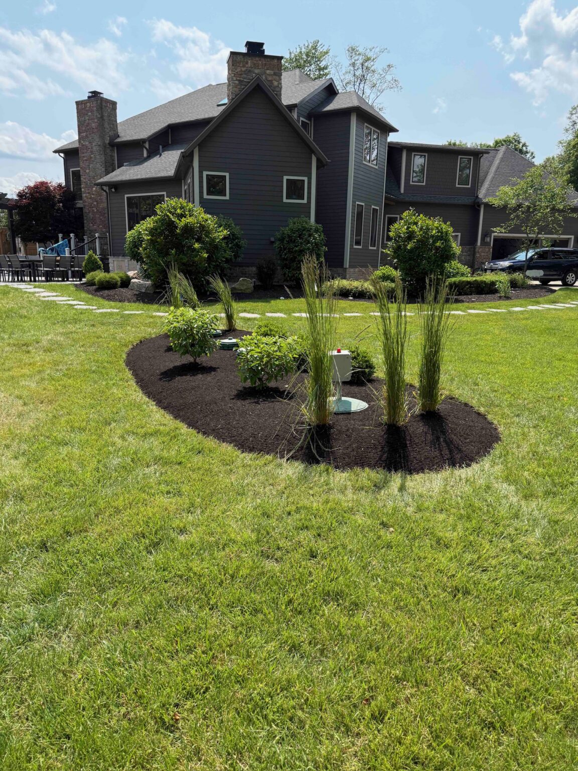 Landscape design and build around septic access with curved planting beds, ornamental grasses, shrubs, mulch, and maintained lawn in Hinckley, Ohio.